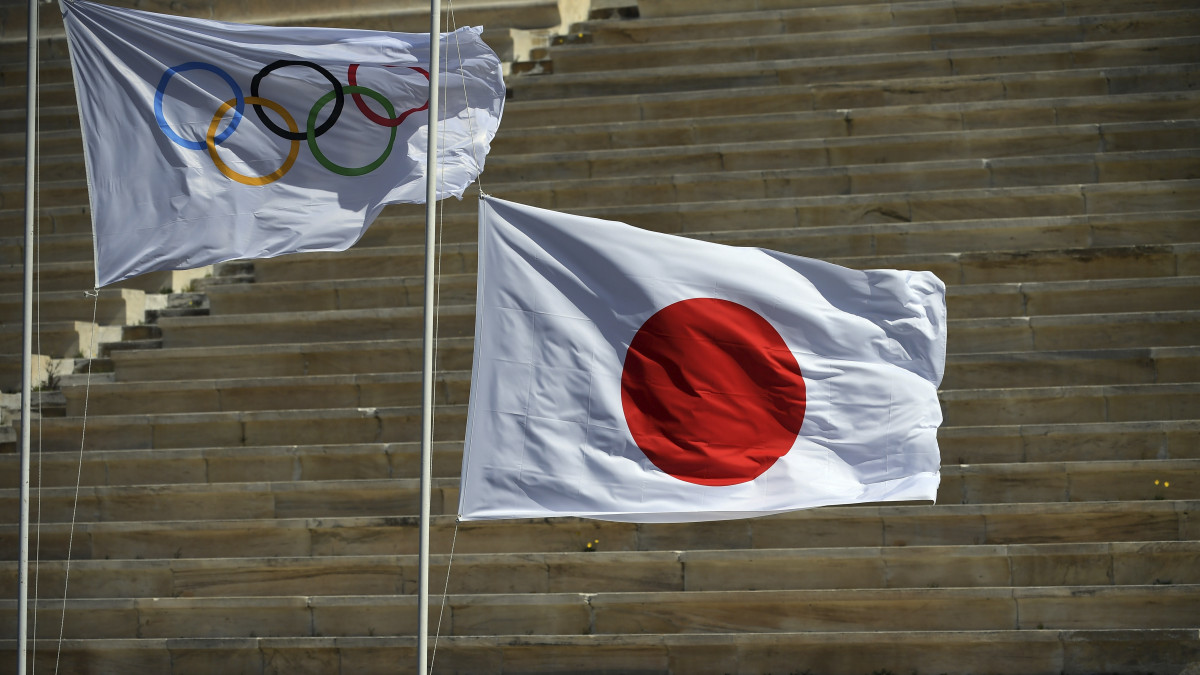 Felhúzzák a japán zászlót az olimpiai zászló mellé az olimpiai láng átadási ünnepségén Athénban 2020. március 19-én. A koronavírus-járvány miatt nézők és delegációk részvétele nélkül megrendezett eseményen a tokiói nyári játékok szervezőbizottságának képviseletében Imoto Naoko japán úszó vette át az olimpiai lángot. Az ötkarikás játékok jelképét azok a japán szervezők viszik el Távol-Keletre, akik már múlt héten megérkeztek Európába. A tokiói nyári olimpiát a tervek szerint július 24. és augusztus 9. között rendezik meg.