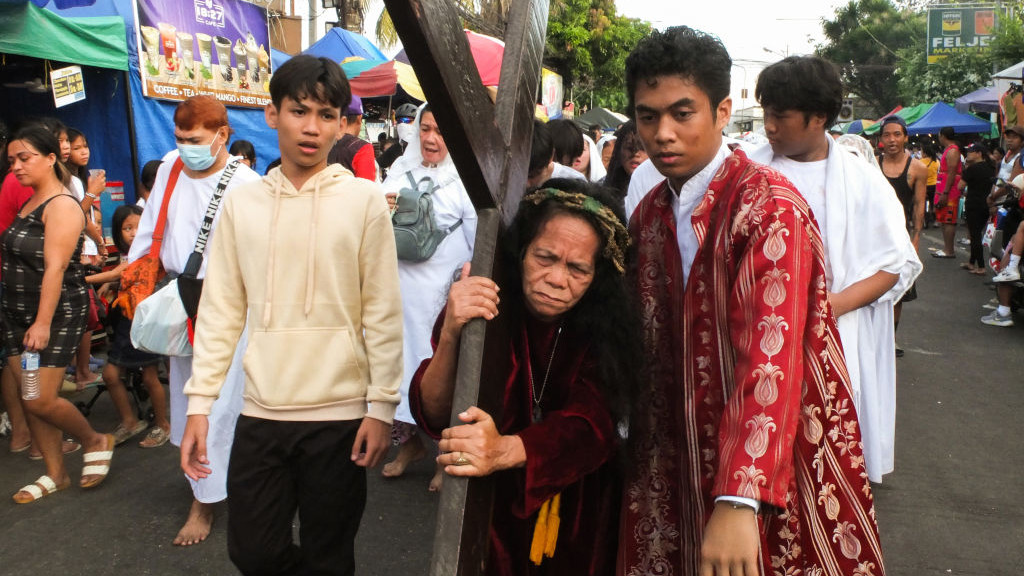 NAVOTAS, PHILIPPINES - 2024/03/29: A woman dressed as Jesus Christ, carrying a cross as an act of penitence. In their way of asking repentance and forgiveness for their sins, flagellants whip their backs by using bamboo strips & get paddled to their buttocks on Good Friday. (Photo by Josefiel Rivera/SOPA Images/LightRocket via Getty Images)