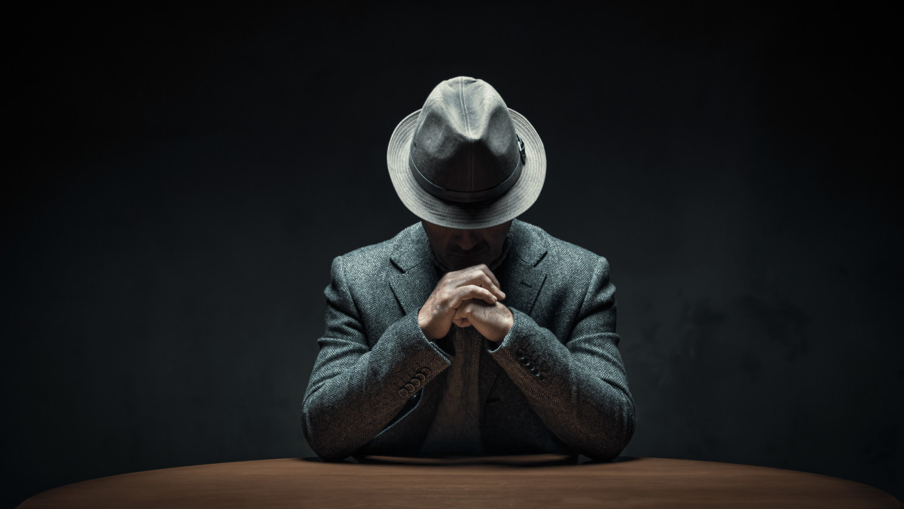 Thoughtful mystery man wearing hat sitting at table in a dark room
