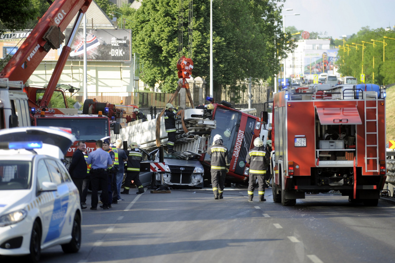 Budapest, 2018. május 3.
Kisbuszra borult tűzoltóautó emelnek daruval a Nagyszőlős utca és a Budaörsi út kereszteződésében 2018. május 3-án. A tűzoltók egy tűzesethez vonultak kék lámpával, szirénázva, amikor oldalára borult a több tíztonnás gépjármű. A kisbuszban egy ember ült, ő a helyszínen meghalt.
MTI Fotó: Mihádák Zoltán