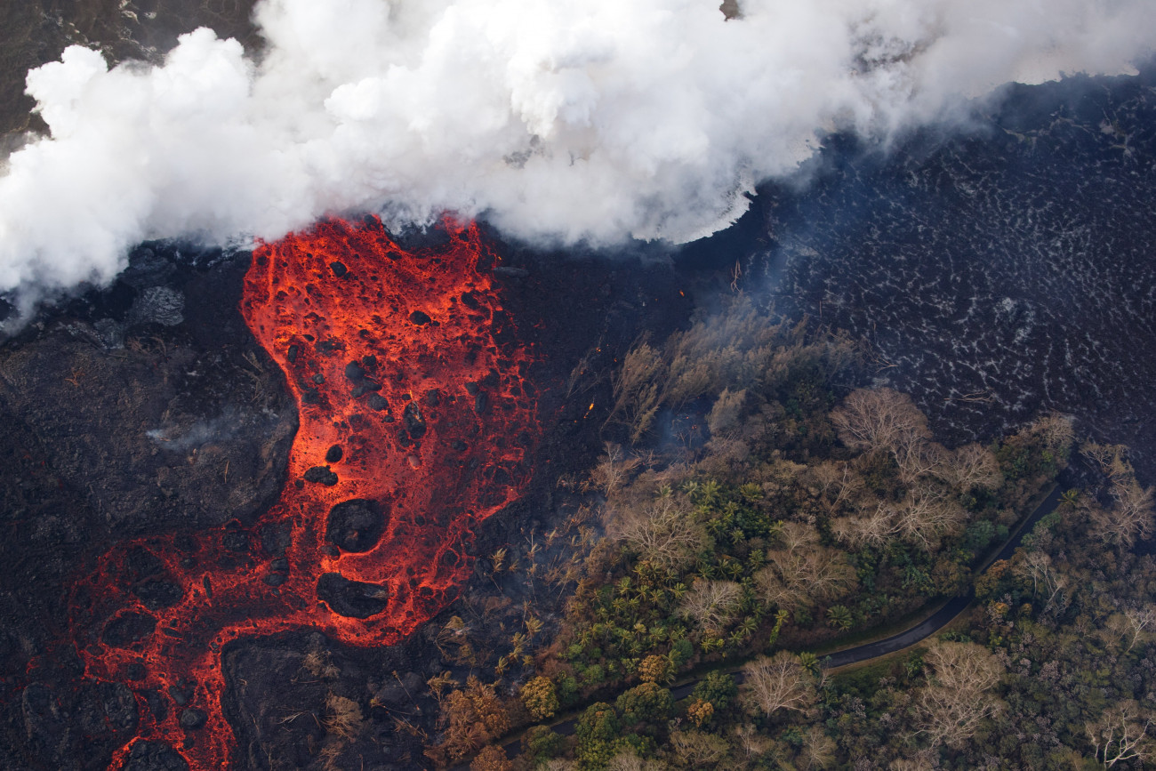 Pahoa, 2018. május 23.
Légi felvétel a Kilauea tűzhányó lávafolyamáról, amint felperzseli az útjában lévő növényzetet a hawaii nagy szigeten fekvő Pahoa város környékén 2018. május 22-én. A világ egyik legaktívabb tűzhányójának számító Kilauea vulkáni tevékenysége május 3. óta tart. A környékén kötelező kitelepítés van érvényben, a lávafolyam eddig 44 házat pusztított el. Jelenleg tilos az óceánban való fürdőzés a térségben, mert a láva és az óceánvíz találkozásakor veszélyes sósav keletkezhet, a vulkán pedig egyre nagyobb mértékben lövell ki szintén mérgező kén-dioxidot. (MTI/EPA/Paradise Helicopters/Bruce Omori)