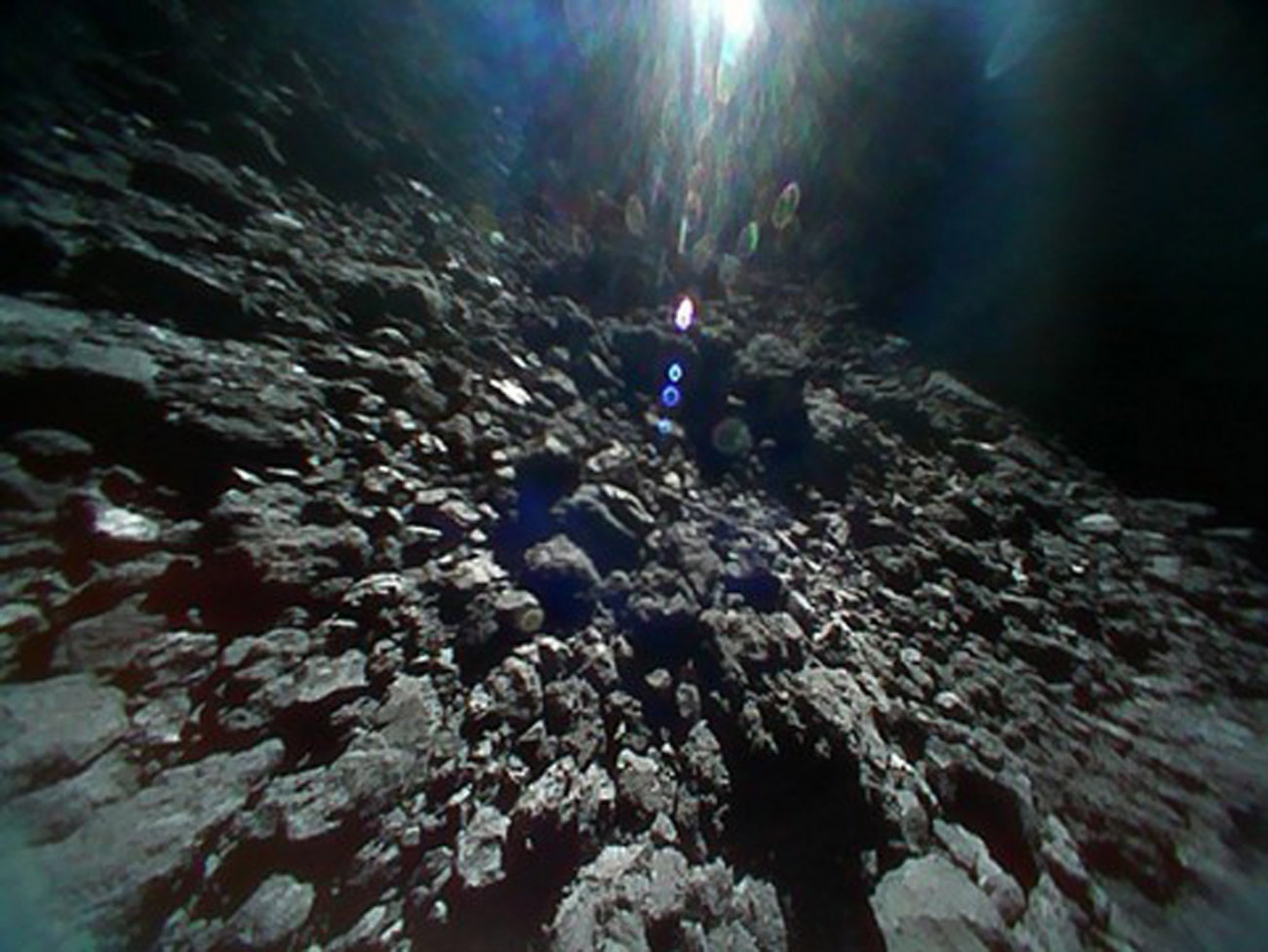 Világűr, 2018. szeptember 28.
A JAXA japán űrügynökség felvétele a Ryugu nevű kisbolygó felszínéről 2018. szeptember 23-án. A felvételt a Hajabusza-2 (Sólyom-2) aszteroidavizsgáló űrszondáról levált, Minerva-2 nevű, robotvezérlésű Rover1B kutatóműszer készítette. A 2014-ben útnak indított Hajabusza-2 űrszonda 2018. június 27-én érte el a Földtől mintegy 280 millió kilométerre levő, egy kilométer átmérőjű Ryugu aszteroidát. A kutatóroverek feladata, hogy felvételeket készítsenek az aszteroidáról, megmérjék a felszíni hőmérsékletét. A csillagászok szerint a Ryugu a Naprendszer hajnalán formálódhatott, így feltételezéseik szerint olyan szerves anyagokat tartalmazhat, amelyek a földi élet kialakulásához is hozzájárulhattak. (MTI/EPA/JAXA)