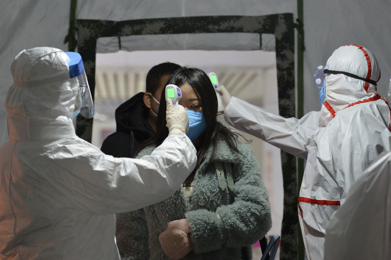 Az utasok testhőmérsékletét ellenőrzik egészségügyi dolgozók az Anhuj kínai tartománybeli Fujang egyik vasútállomásán. Fotó: MTI/AP/Chinatopix