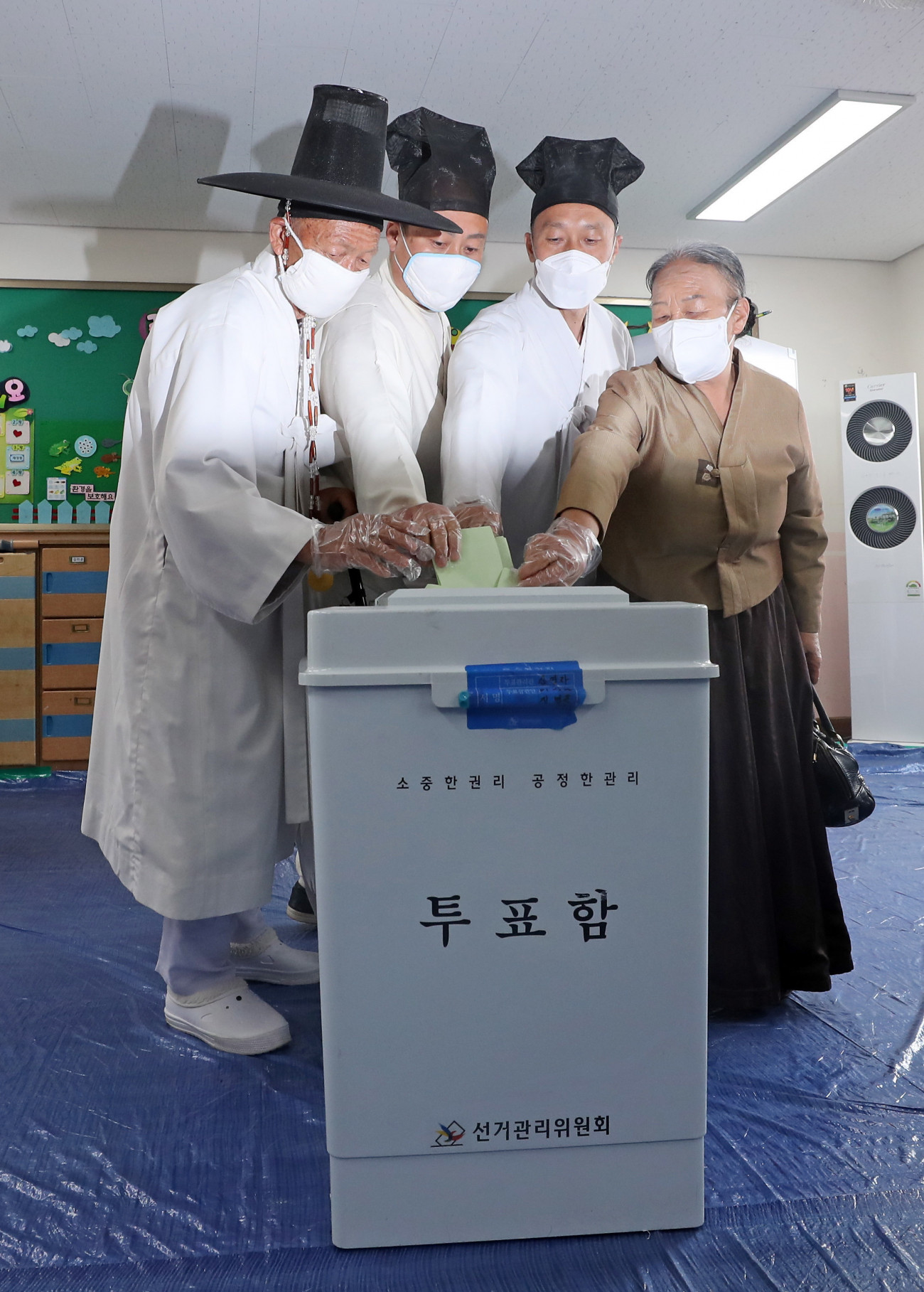 Nonszan, 2020. április 15.
A koronavírus-járvány miatt védőmaszkot viselő Ju Bok Jop, egy hagyományos koreai viseletbe, dopóba öltözött falusi iskolai tanár (b) szavaz a családjával a dél-koreai parlamenti választásokon Nonszanban 2020. április 15-én.
MTI/Yonhap