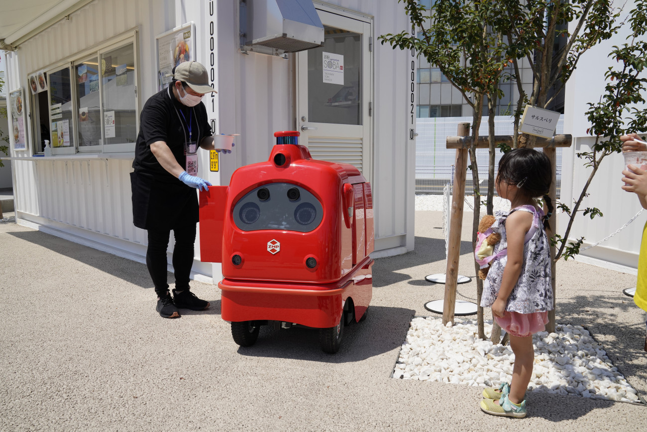 Tokió, 2020. augusztus 12.
Ételt rak be a gép dobozába egy büfé dolgozója DeliRo, a házhozszállító robot próbaüzeme alatt Tokióban 2020. augusztus 12-én. A ZMP japán robottechnikai vállalat által kifejlesztett gép az interneten leadott rendelések alapján képes egy élelmiszerboltból a vásárlóhoz szállítani az árut, amelyet célba érkezése után okostelefon alkalmazásával a dobozából lehet kivenni. DeliRo a beléépített kamerák és lézeres érzékelők segítségével tud közlekedni óránként 6 kilométeres sebességgel.
MTI/EPA/Majama Kimimasza