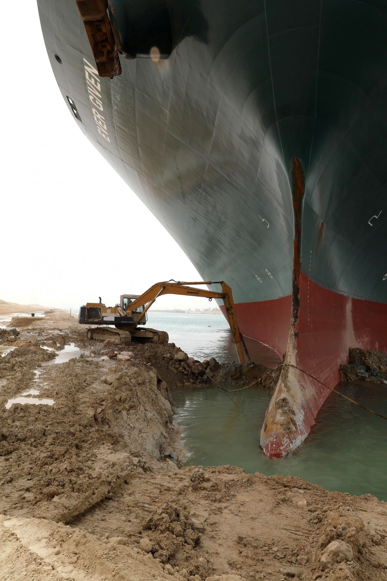 Szuezi-csatorna, 2021. március 25.
A Szuezi-csatorna Hatóság által közreadott képen munkagéppel próbálják kiszabadítani a keresztbe fordult és beszorult Ever Given nevű konténerszállítót a Szuezi-csatornában 2021. március 25-én. A világ egyik legnagyobb teherhajója egy napja blokkolja a forgalmat, a baleset miatt felfüggesztették a hajóforgalmat a Szuezi-csatornában.
MTI/EPA/Szuezi-csatorna Hatóság