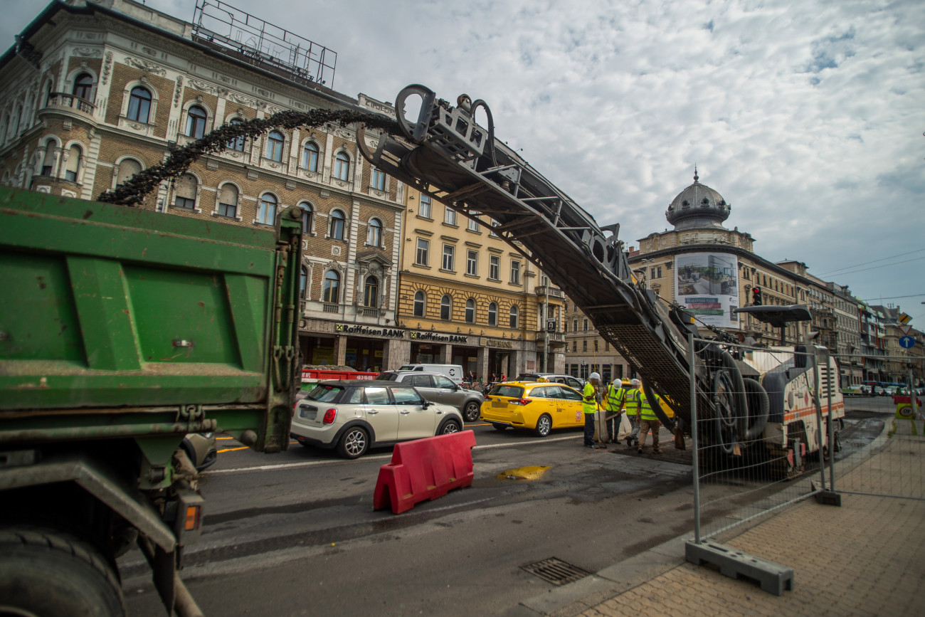 Budapest, 2021. július 12.
Autók közlekednek az aszfaltot felmaró munkagép mellett a felújítás alatt álló fővárosi Blaha Lujza térnél 2021. július 12-én. Ezen a napon megkezdődtek a munkálatok téren. Az első ütemben az aluljáró födémjét szigetelik, ezért 10-12 hétig komolyabb forgalomkorlátozásra kell számítani a csomópontban. A tér felújítása várhatóan 2022 végére fejeződik be.
MTI/Balogh Zoltán