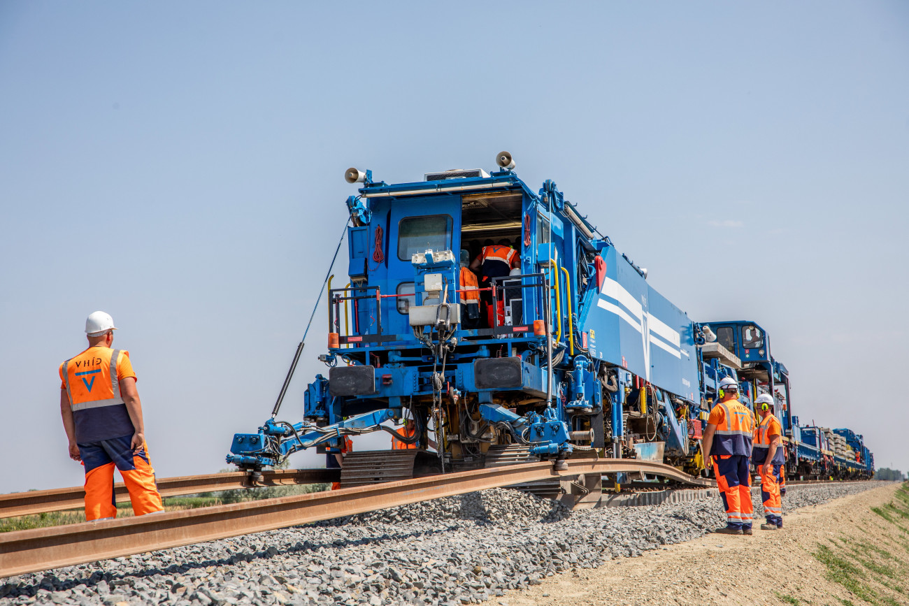 Röszke, 2022. július 3.
A világ egyik legnagyobb vasútépítőgép-gyártója, a Plasser & Theurer által épített SMD-80/UVP2002 típusú vágányépítő és átépítő géplánc a Szeged és a röszkei határ vasútvonal-fejlesztés kivitelezési munkáinak jelenlegi állásáról tartott sajtótájékoztató után Röszkén 2022. július 3-án. A magyar kormány 45 milliárd forintot költ hazai költségvetési forrásból arra, hogy Szeged és a röszkei határ között egyvágányú, villamosított, óránként 120 kilométeres sebességre alkalmas új vasúti pálya épüljön.
MTI/Rosta Tibor