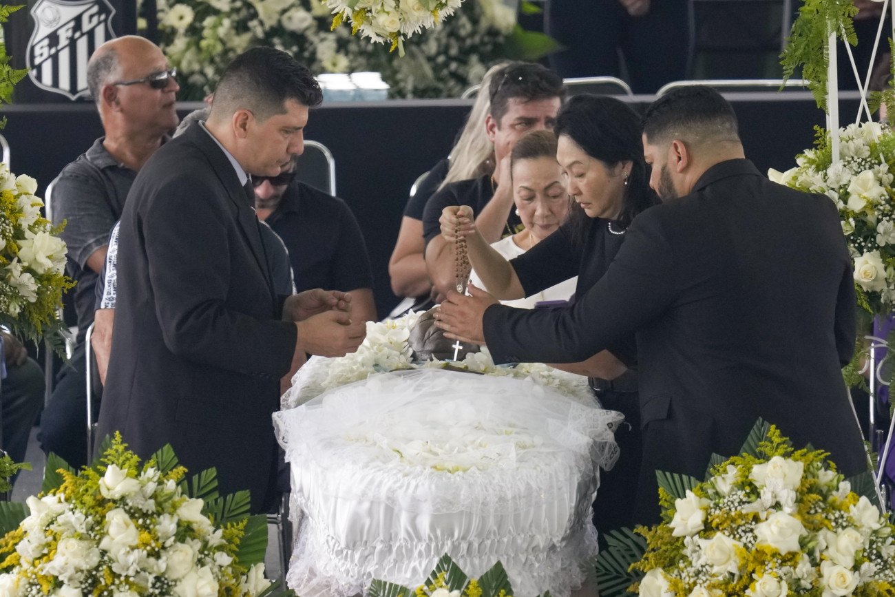 Santos, 2023. január 2.
Marcia Aoki, Edson Arantes do Nascimento, közismert nevén Pelé háromszoros világbajnok brazil labdarúgó özvegye (j2) egy rózsafüzért helyez a férje holttestére a santosi Vila Belmiro stadionban felállított ravatalnál 2023. január 2-án. A ravatal előtt 24 órán keresztül bárki leróhatja kegyeletét, temetése január 3-án lesz. Pelé 2022. december 29-én, 82 éves korában hunyt el. Jair Bolsonaro, a hivatalából távozó brazil elnök háromnapos nemzeti gyászt rendelt el a tiszteletére.
MTI/AP/Andre Penner