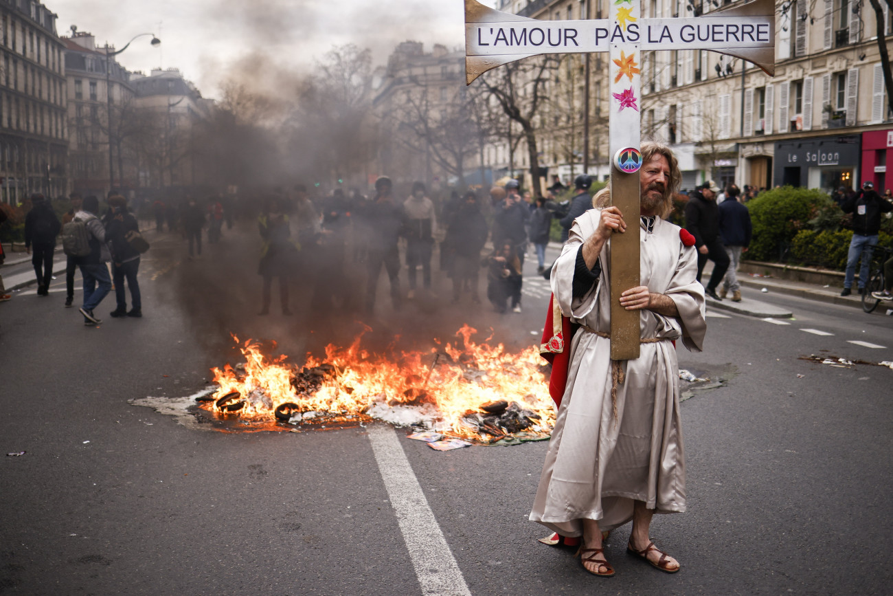 Párizs, 2023. március 28.
A nyugdíjreform ellen tüntetők egyike szerelmet, ne háborút jelentésű feliratot viselő kereszttel Párizsban 2023. március 28-án. Emmanuel Macron francia elnök széles körű felháborodást váltott ki azzal, hogy parlamenti szavazás nélkül készül hatályba léptetni a nyugdíjkorhatár 62-ről 64 évre emelését előirányzó törvényt.
MTI/EPA/Yoan Valat