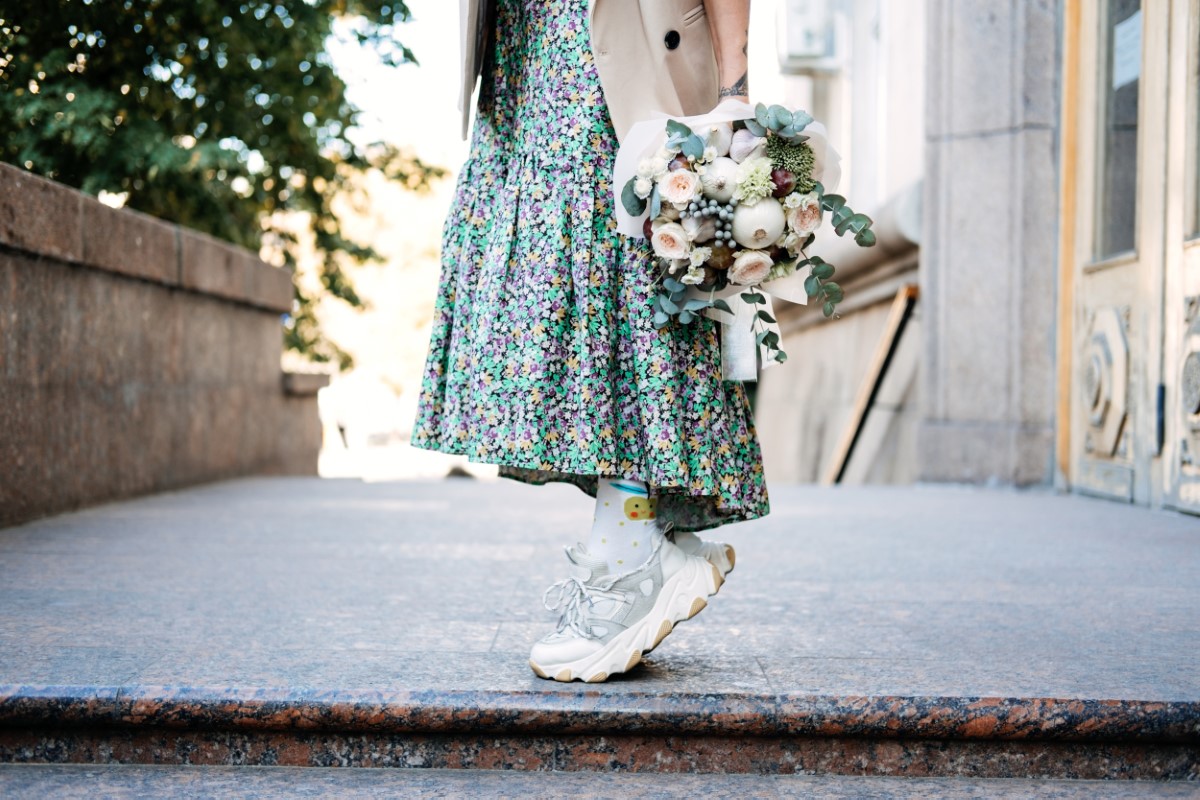 Contemporary modern trendy Hipster bride in informal dress and sneakers with Edible Wedding Bridal Flower Bouquet. Modern gen z Bride leg in comfortable shoe sneakers.