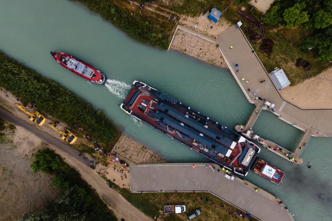Siófok, 2023. június 28.
A drónnal készült felvételen a Balatoni Hajózási Zrt. (Bahart) egyik új kompját vontatják a Sió-csatorna balatonkiliti duzzasztógátjánál 2023. június 28-án. A Bahart a Magyar Turisztikai Ügynökség (MTÜ) közreműködésével építtetett két új személyhajója és két kompja 2021-ben készült el a komáromi hajógyárban, ahonnan egy héttel ezelőtt indultak útnak, hogy a Dunán lehajózva a Sió-csatornán keresztül elérjék a Balatont.
MTI/Vasvári Tamás