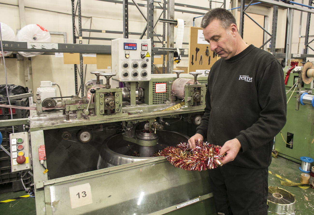 CWMBRAN, WALES - DECEMBER 10:  Festive employee Jason Poulsom inspects freshly made tinsel samples in the factory area of the Festive Productions Ltd premises on December 10, 2013 in Cwmbran, Wales. Although Christmas Day 2013 is only two weeks away, the staff at Festive are already planning and gearing up for Christmas 2014. The 14 acre fully integrated showroom, factory and warehouse measuring 250000 sq ft in size holds Festive Productions, who are now the last manufacturer of tinsel in UK - with the majority of tinsel sold in the UK made at the factory in Wales. As well as tinsel, Festive, which is one of Europe's largest suppliers and manufacturer of Christmas and seasonal decorations, has increased its product portfolio, to include nearly every conceivable Christmas decoration category including baubles, tinsel garlands, wreaths, lights, fibre optic trees and artificial trees.  (Photo by Matt Cardy/Getty Images)