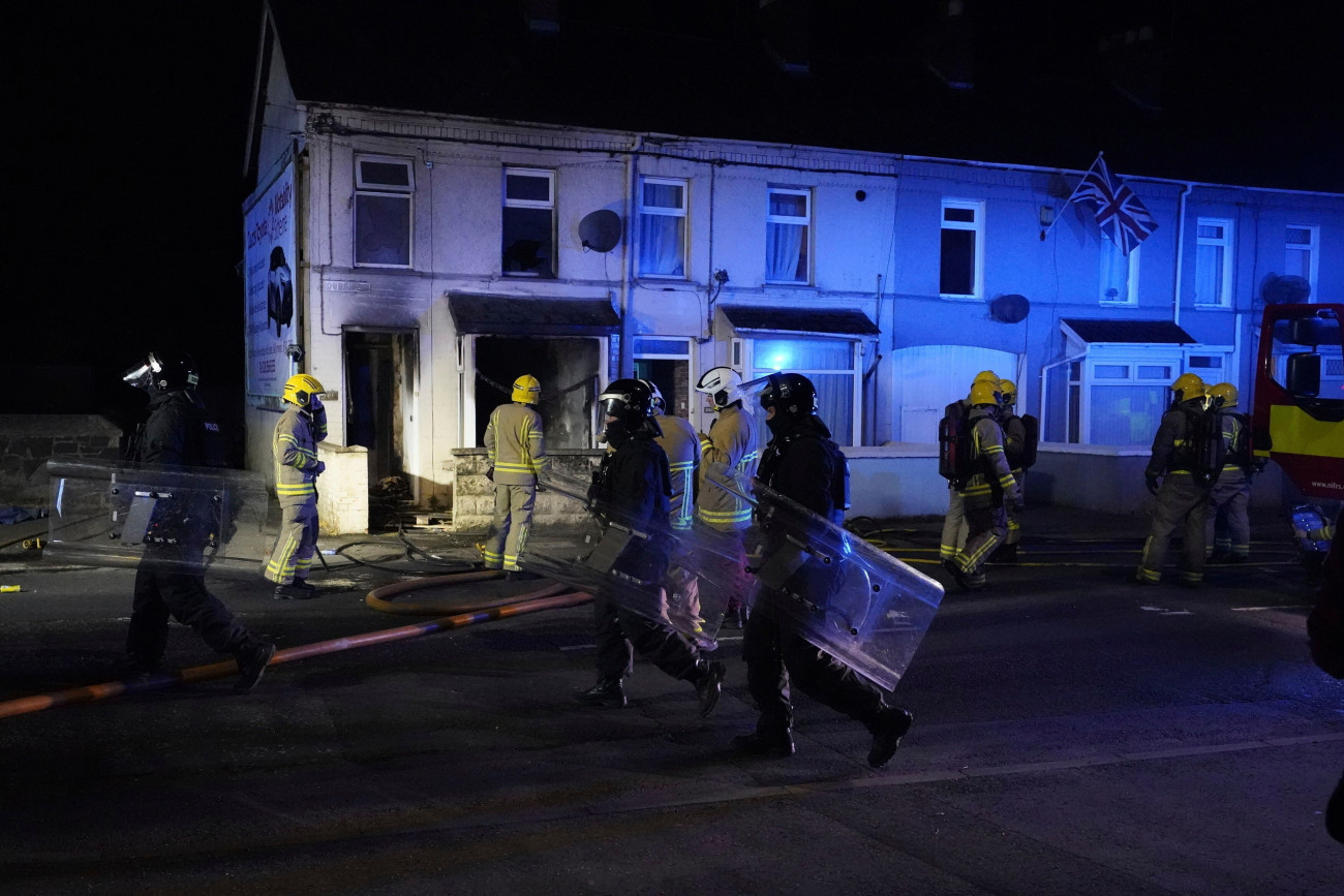 Ballymena, 2025. június 11.
Rohamrendőrök és tűzoltók az észak-írországi Ballymena városában, ahol zavargások törtek ki egy bevándorlók által elkövetett szexuális támadás miatt 2025. június 10-én. Az indulatok azt követően szabadultak el, hogy két 14 éves román bevándorló fiatal megpróbált megerőszakolni egy helyi lányt.
MTI/AP/PA/Niall Carson