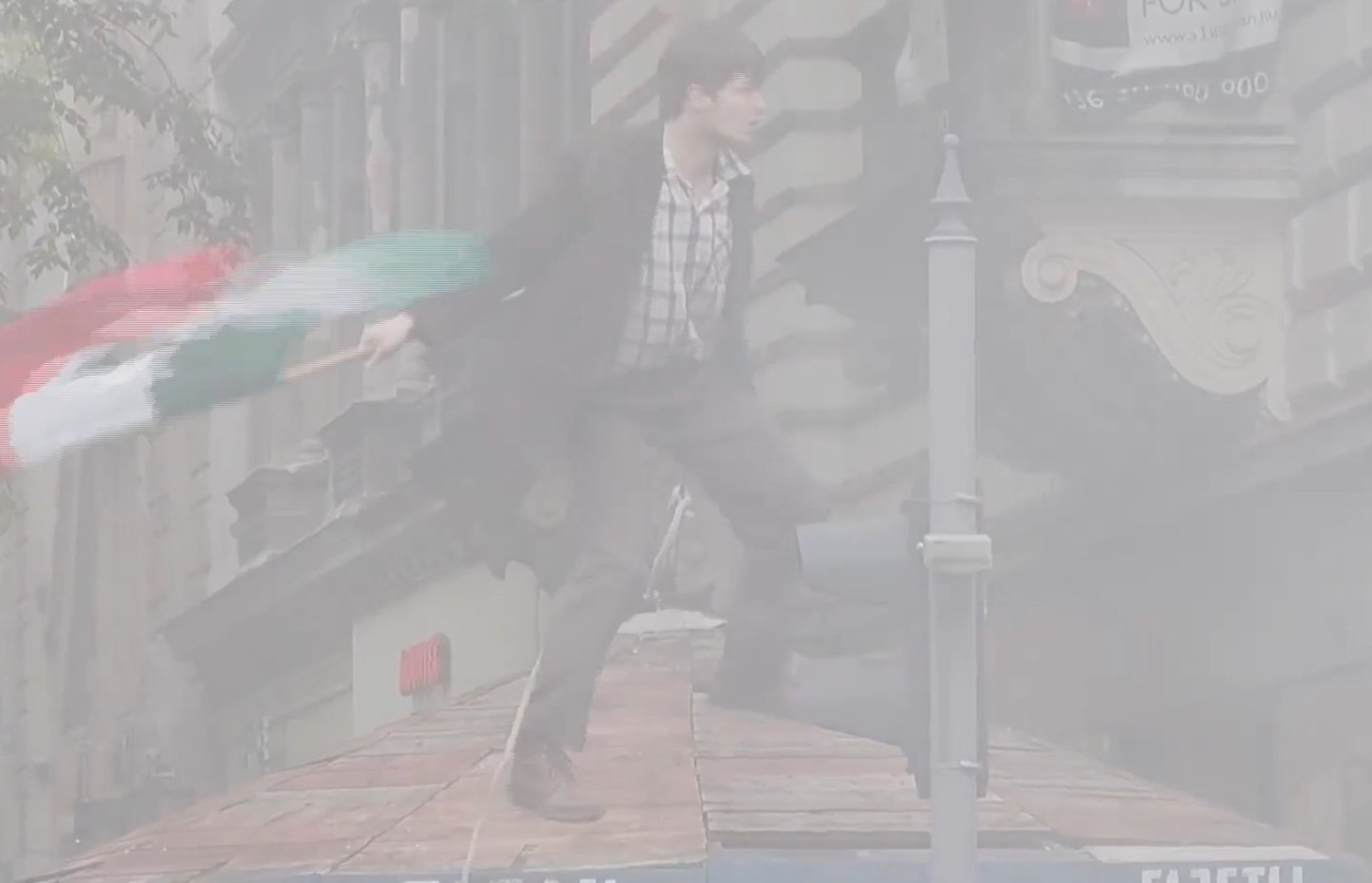 Lyukas magyar zászlót lenget egy férfi egy Molotov-koktél füstjében egy 