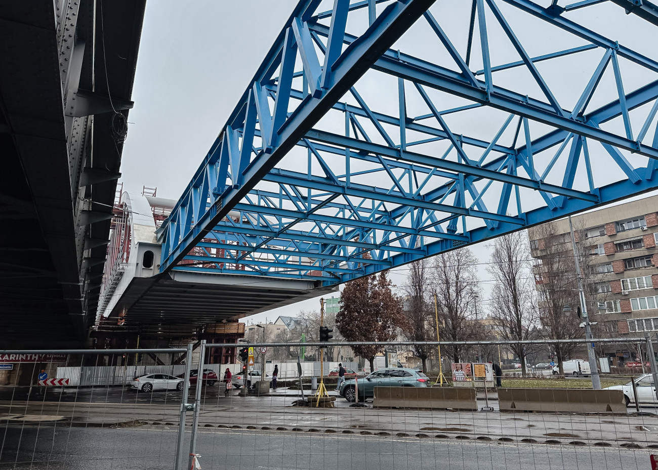 Budapest, 2026. február 2.
Az újonnan összeszerelt kétszer kétvágányos acélhíd elsõ szerkezeti eleme és az áttoláshoz használt segédszerelvénye a helyére illesztése elõtt a Bartók Béla úti közúti-vasúti átjárónál 2026. február 2-án. A fejlesztés része a Kelenföld és Ferencváros közötti vasútvonal kapacitásbõvítésének, amely a Déli Körvasút kialakításának második üteméhez kapcsolódik.
MTI/Hatházi Tamás