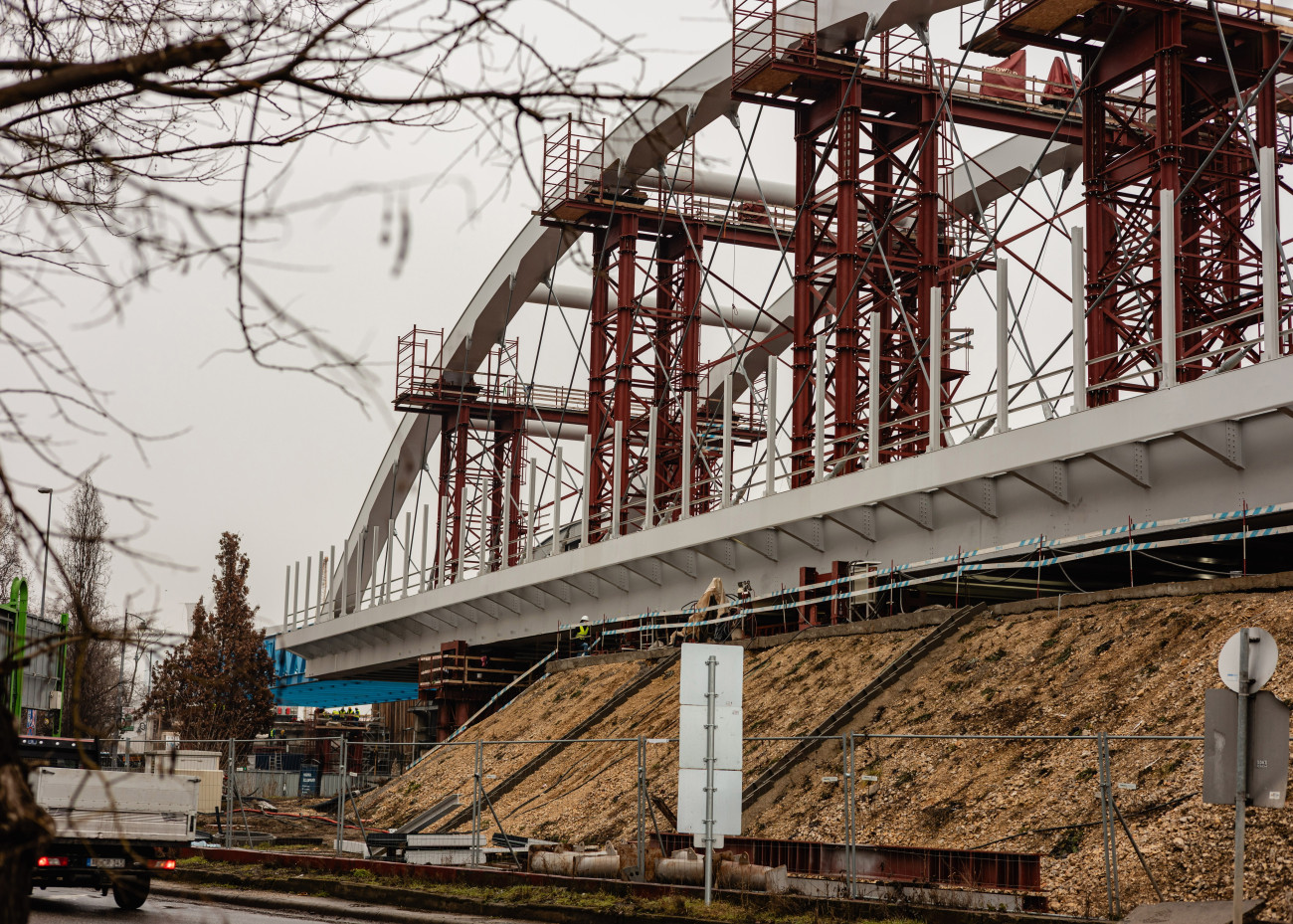 Budapest, 2026. február 2.
Az újonnan összeszerelt kétszer kétvágányos acélhíd elsõ szerkezeti eleme a helyére illesztése elõtt a Bartók Béla úti közúti-vasúti átjárónál 2026. február 2-án. A fejlesztés része a Kelenföld és Ferencváros közötti vasútvonal kapacitásbõvítésének, amely a Déli Körvasút kialakításának második üteméhez kapcsolódik.
MTI/Hatházi Tamás