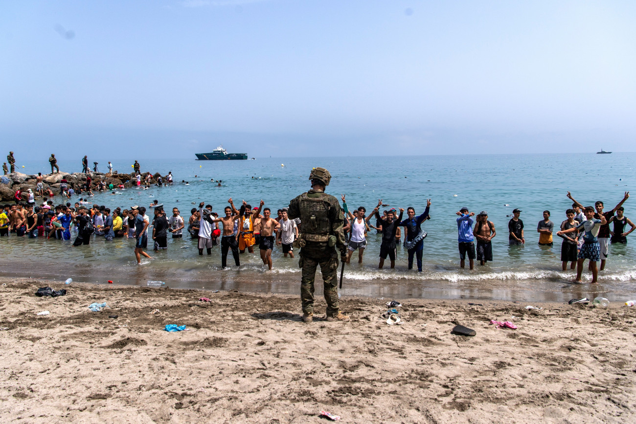 Ceuta, 2026. július 31.
A Spanyolországhoz tartozó Ceutába bejutni próbáló migránsok elõtt a tengerpartot lezáró spanyol katona 2026. július 31-én. Az elõzõ napokban spanyol médiajelentések szerint mintegy ötvenezer ember érkezett illegálisan Marokkóból az észak-afrikai ország területébe ékelõdõ spanyol exklávéba.
MTI/AP/Antonio Sempere