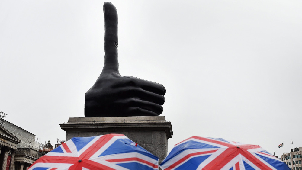 London, 2016. szeptember 29.David Shrigley brit képzőművész Really Good (Nagyon jó) című, aránytalanul hosszú hüvelykujjat formázó bronzszobrát nézik esernyős érdeklődők a londoni Trafalgar téren 2016. szeptember 29-én, miután Sadiq Khan londoni polgármester leleplezte a 7 méter magas alkotást. Az 1844-ben átadott tér négy sarkában álló szobortalpak közül az egyetlen üresen maradt alapzaton 1999 óta a brit Királyi Művészeti Társaság (RSA), majd az erre a célra 2005-ben létrejött bizottság kortárs képzőművészek szobrait állítja ki. (MTI/EPA/Andy Rain)