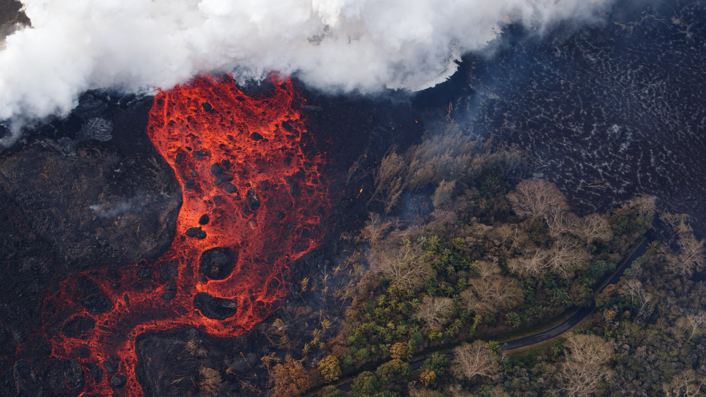 Pahoa, 2018. május 23.Légi felvétel a Kilauea tűzhányó lávafolyamáról, amint felperzseli az útjában lévő növényzetet a hawaii nagy szigeten fekvő Pahoa város környékén 2018. május 22-én. A világ egyik legaktívabb tűzhányójának számító Kilauea vulkáni tevékenysége május 3. óta tart. A környékén kötelező kitelepítés van érvényben, a lávafolyam eddig 44 házat pusztított el. Jelenleg tilos az óceánban való fürdőzés a térségben, mert a láva és az óceánvíz találkozásakor veszélyes sósav keletkezhet, a vulkán pedig egyre nagyobb mértékben lövell ki szintén mérgező kén-dioxidot. (MTI/EPA/Paradise Helicopters/Bruce Omori)