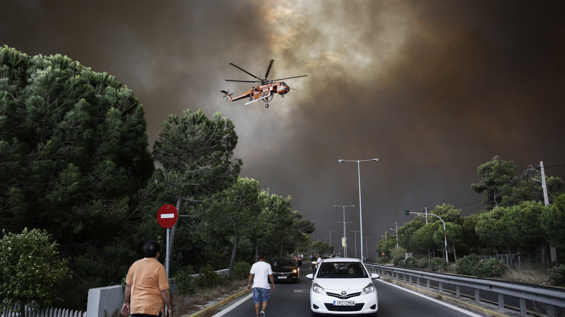 Athén, 2018. július 23.A görög fővárostól északkeletre pusztító erdőtűz ellen küzdő tűzoltó-helikopter egy athéni külvároson át húzódó autópálya fölött 2018. július 23-án. Az Athén és Korinthosz közötti tengerparti település, Kineta melletti Geraneia hegyen keletkezett tűz után újabb erdőtűz lobbant fel a fővárostól északkeletre fekvő Penteli-hegyen. (MTI/EPA/Alexandrosz Vlahosz)