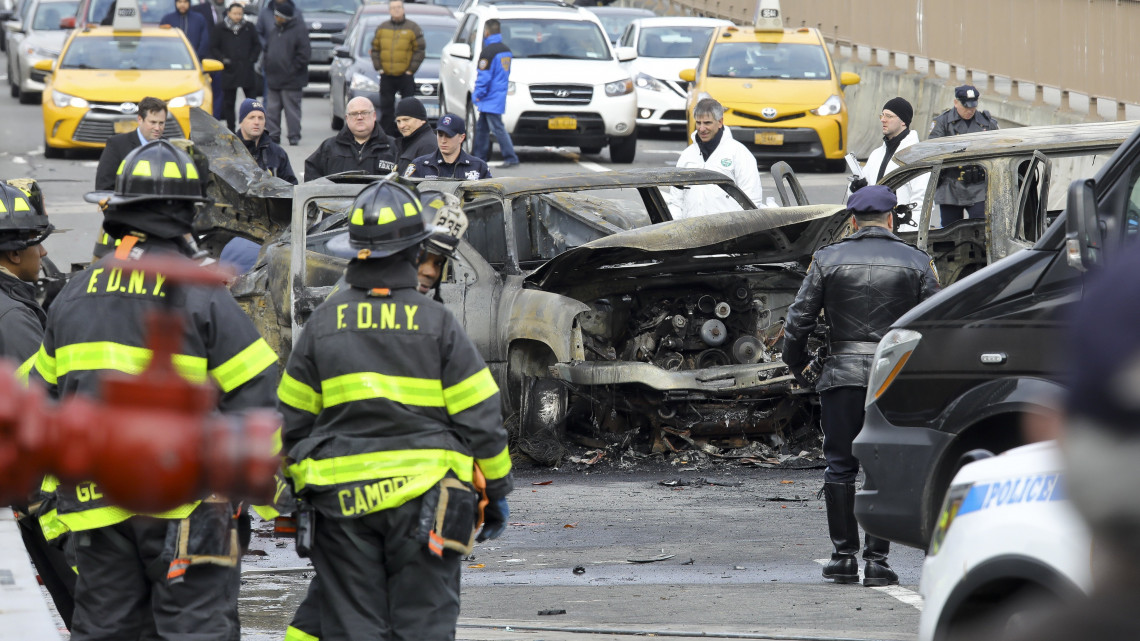 Rendőrök és tűzoltók vizsgálják a kiégett autóroncsokat a Manhattan szigetét és New York Brooklyn nevű városrészét összekötő Brooklyn hídon 2018. november 21-én. A közúti balesetben egy ember életét vesztette, hatan megsérültek.