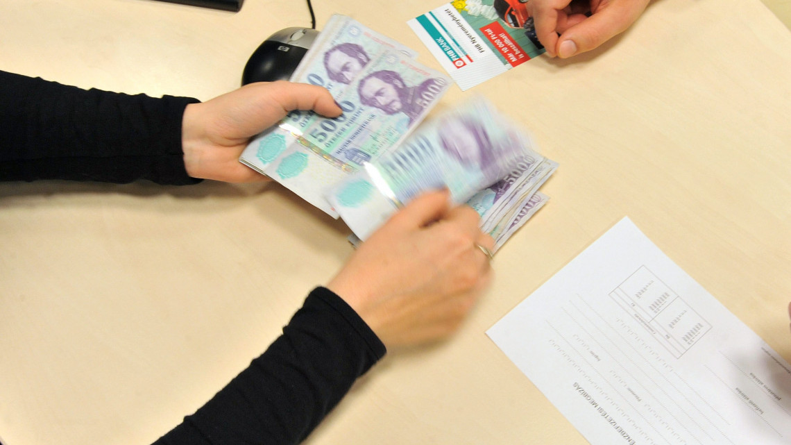 Egy banki alkalmazott készpénzt vesz át egy ügyféltől, aki ötezer forintosokkal fizet az FHB Bank XIII. kerületi Váci úti bankfiókjában.