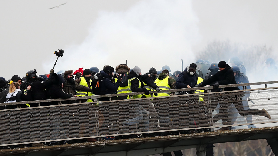 Rohamrendőrök és a sárgamellényesek összecsapása Párizsban 2019. január 5-én. A pártfüggetlen sárgamellényes mozgalom november közepén szerveződött Franciaországban az üzemanyagadó emelése ellen. A november 17. óta tüntető sárgamellényesek azóta egyre több szociális jellegű követelést fogalmaznak meg, és Emmanuel Macron államfő távozását követelik.