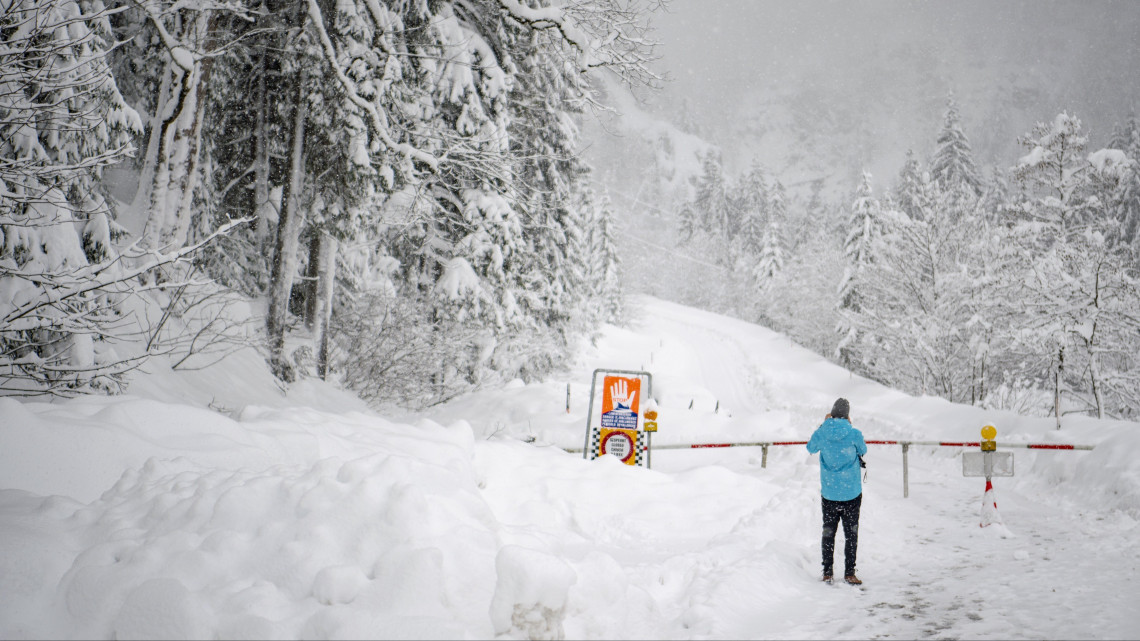 Lavinaveszélyre figyelmeztető táblát fényképez egy férfi az erős hóesésben egy lezárt útnál, az ausztriai Untertauern közelében 2019. január 7-én.