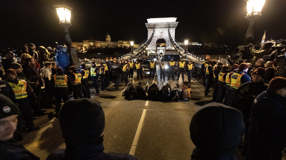 Tüntetők ülnek az úttesten a munka törvénykönyvének az önkéntes túlmunkaidő bővítéséről szóló módosítása elleni demonstráció után a Lánchíd pesti hídfőjénél 2019. január 19-én. A tüntetők a Várkert Bazárnál megtartott demonstráció befejezése után vonultak a hídfőhöz.