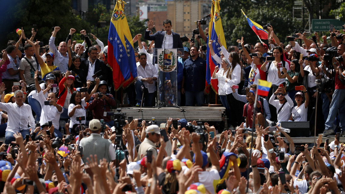 Ellenzéki tüntetők éltetik Juan Guaidót, a venezuelai ellenzéki többségű parlament elnökét (középen, az emelvényen), aki ideiglenes elnökké nyilvánította magát a hivatalban lévő államfő, Nicolás Maduro elleni tüntetésen Caracasban 2019. január 23-án.
