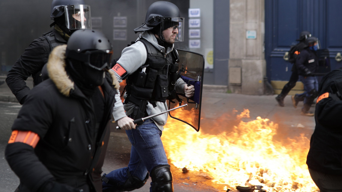 A francia kormány szociális és adópolitikája ellen tiltakozó sárgamellényesek által felgyújtott kukák mellett futnak el rohamrendőrök Párizsban 2019. február 9-én. Ez a tüntetések egymás utáni tizenharmadik hétvégéje.