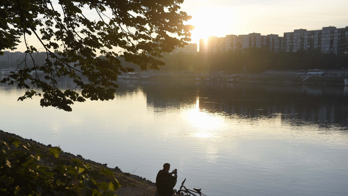 Telefonját nézi letámasztott kerékpárja mellett egy férfi a Duna partján a fővárosi Margitszigeten 2018. május 26-án reggel.