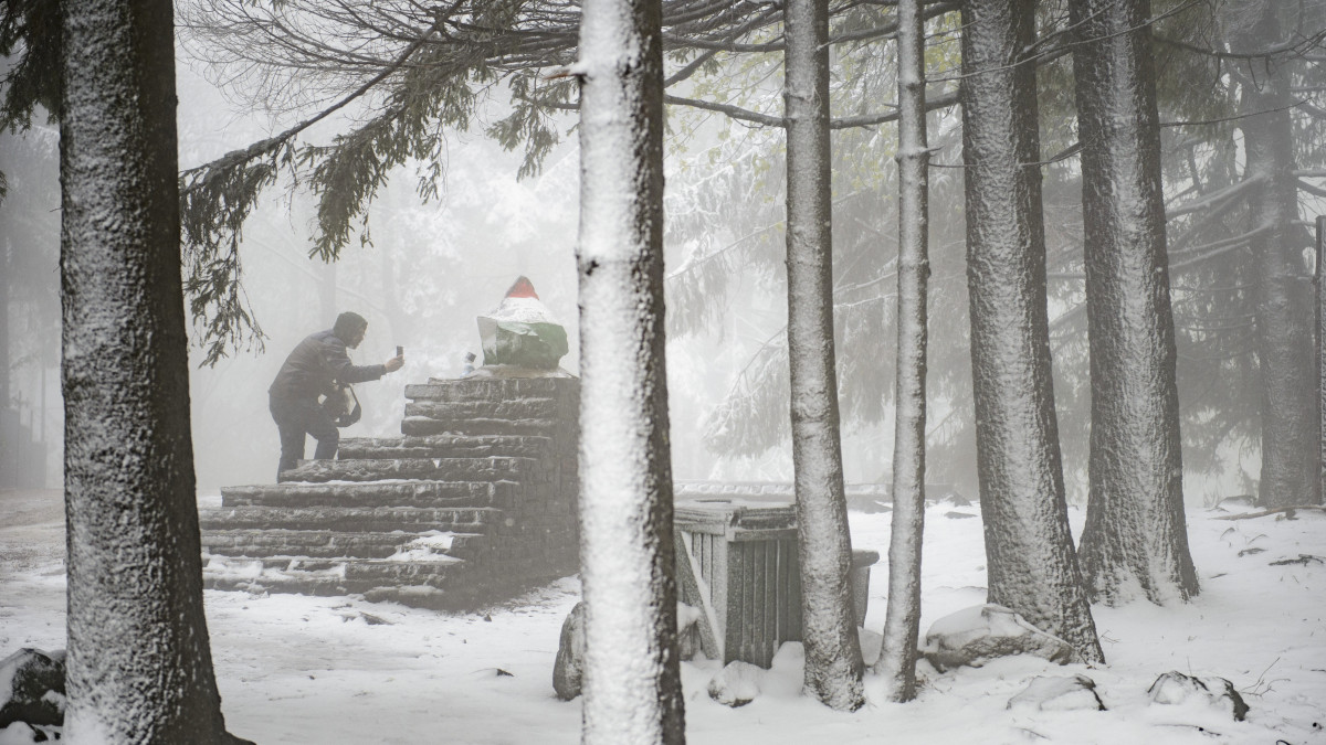 Fényképet készít egy férfi a Kékes csúcsát jelölő kőről a hóesésben 2019. május 6-án.