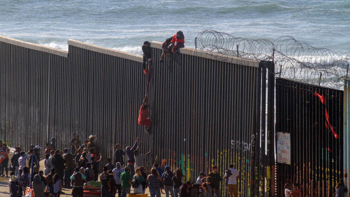 Menekültek próbálnak átjutni a mexikói-amerikai határkerítésen a Baja California mexikói állambeli Tijuana tengerpartján 2019. március 19-én.