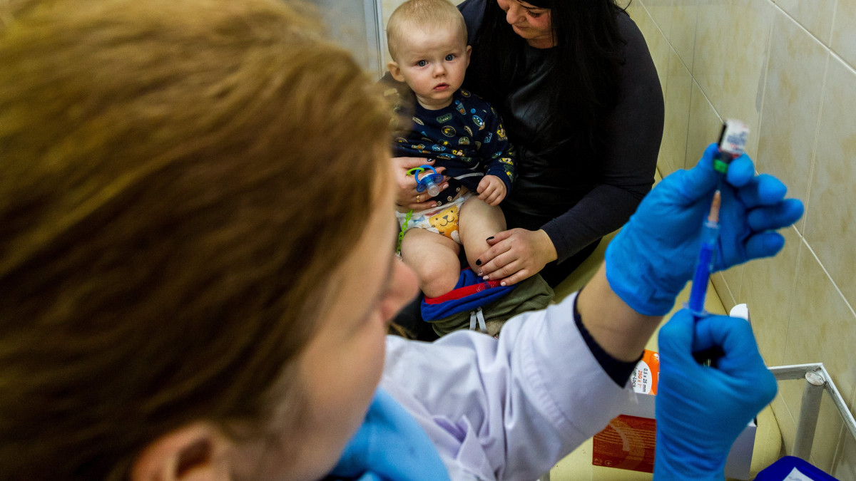 Kisgyermek édesanyja ölében ülve várja, hogy kanyaró elleni védőoltást kapjon az egyik háziorvosi rendelőben a kárpátaljai Ungváron 2018. február 1-jén. Január végén nyolcezer adag, a veszélyes, fertőző betegség elleni oltóanyagot adott át a magyar kormány humanitárius gyorssegélyként több mint 100 millió forint értékben Grezsa István, Kárpátaljáért felelős kormánybiztos Ungváron az Ukrán Vöröskereszt Kárpátalja megyei szervezetének.