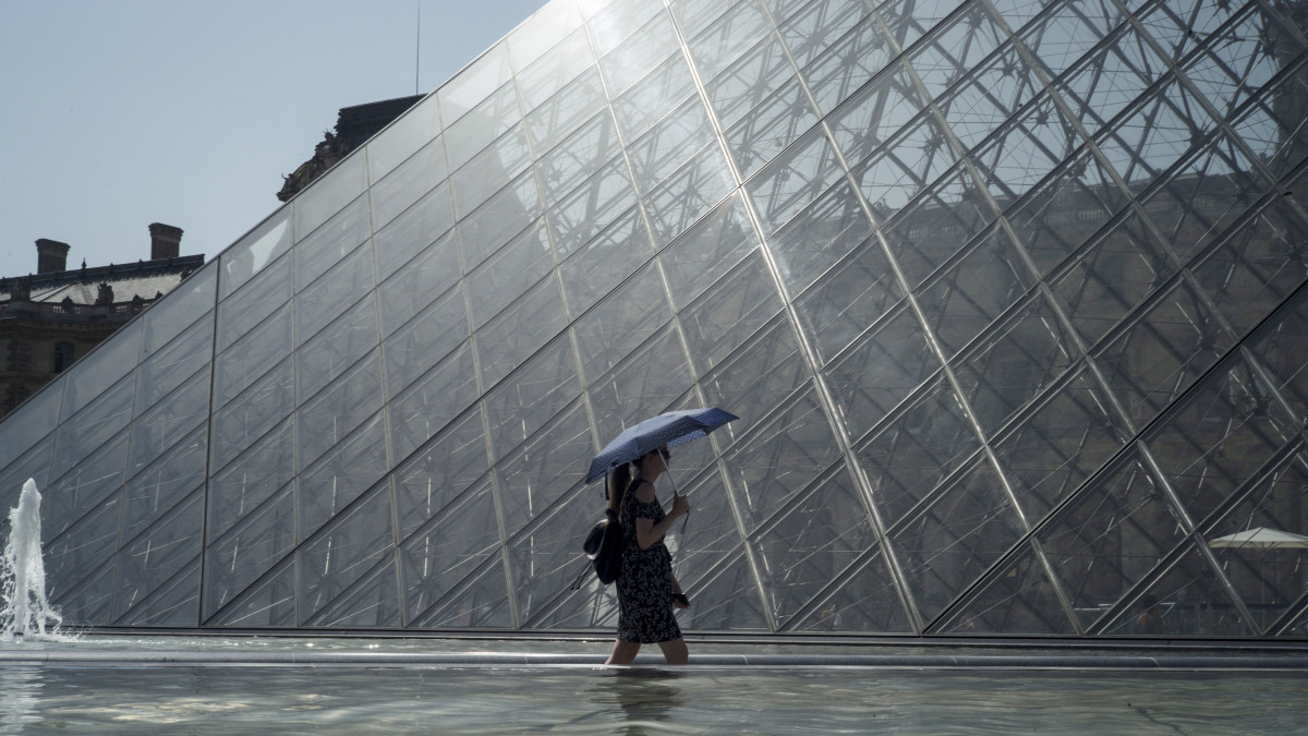 Ernyővel sétáló nő a párizsi Louvre előtti szökőkútnál 2019. július 25-én. A francia meteorológiai szolgálat közlése szerint Párizsban ezen a napon megdőlt a több mint hetvenéves abszolút melegrekord 41 fokkal.