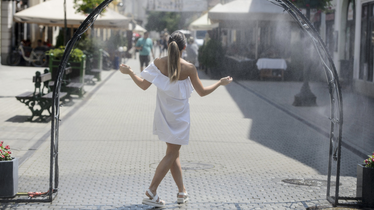 Fiatal nő egy párakapunál hűti magát a hőségben az egri Széchenyi István utcában 2019. június 26-án. A hőség miatt az egész országra figyelmeztetéseket adott ki az Országos Meteorológiai Szolgálat.