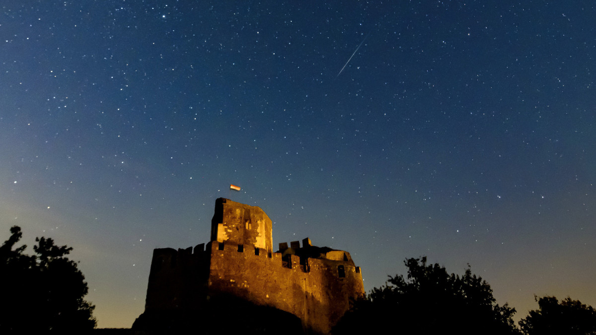 Meteor az égbolton a hollókői vár felett 2019. augusztus 12-re virradóan. A Föld belépett a Perseida meteorraj összetevőit alkotó 109P/Swift-Tuttle üstökös pályája mentén szétszórt porfelhőbe. A Perseidák az egyik legismertebb, sűrű csillaghullást előidéző meteorraj.