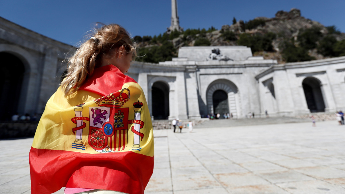 San Lorenzo del Escorial, 2018. augusztus 21.A spanyol zászlóba burkolózik egy nő a spanyol polgárháború áldozatainak emléket állító Elesettek Völgyében, a Madridtól 40 kilométerre fekvő San Lorenzo del Escorialnál 2018. augusztus 21-én. A júniusban hivatalba lépett szocialista spanyol kormány arra készül, hogy kihantoltatja és eltávolíttatja Francisco Franco egykori spanyol diktátor földi maradványait az Elesettek Völgyében lévő katolikus bazilikából. (MTI/EPA/Mariscal)