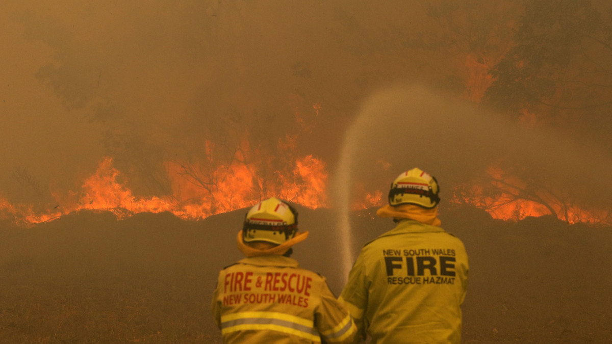 Tűzoltók küzdenek a lángok megfékezésén az Új-Dél-Wales állambeli Old Bar település közelében 2019. november 9-én. Új-Dél-Walesben 72 bozóttűz volt aktív, ezek közül 18-at egyelőre nem tudtak megfékezni, és hat veszélyeztet lakott területet. Az államban legkevesebb két ember életét vesztette, több százezer hektárnyi terület égett le.