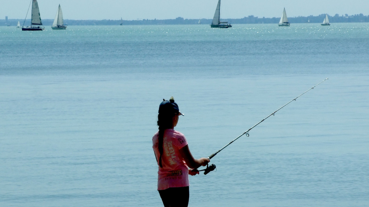 Egy tizenéves sporthorgász lány próbál szerencsét a Balaton-partról. Távolabb vitorlás sporthajók és jachtok a tó vizén. MTVA/Bizományosi: Jászai Csaba  *************************** Kedves Felhasználó!