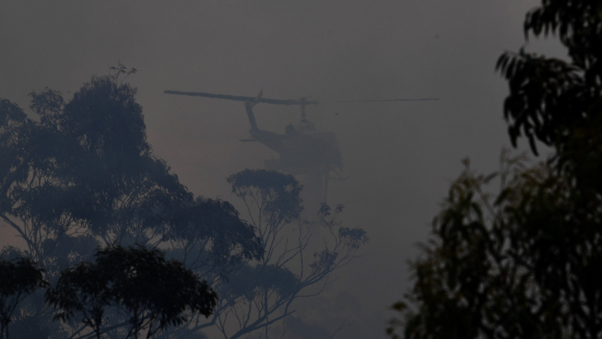 Helikopter az Új-Dél-Wales állambeli Bilpin közelében pusztító bozóttűz füstjében 2019. december 7-én. Az elhúzódó aszály sújtotta kontinensország keleti partvidékén hetek óta pusztítanak bozóttüzek.