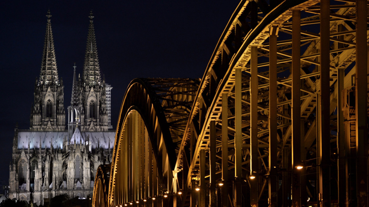 Köln, 2017. augusztus 8.Alulról világítják meg a Hohenzollern-híd szerkezetét a Kölni dóm tornyainak előterében az észak-rajna-vesztfáliai nagyvárosban 2017. augusztus 7-én. (MTI/EPA/Sascha Steinbach)