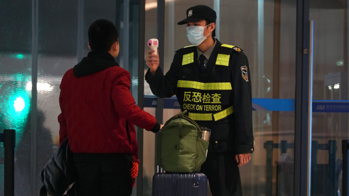 Infravörös hőmérővel méri egy távozó utas testhőmérsékletét egy dolgozó a vuhani nemzetközi repülőtéren 2020. január 21-én. A Pekingben és a dél-kínai Sencsenben is felbukkant új, tüdőgyulladást okozó vírus kiindulópontjának számító közép-kínai Vuhanban jelentősen megugrott a fertőzöttek száma, a vírusfertőzés eddig legkevesebb négy ember halálát okozta.