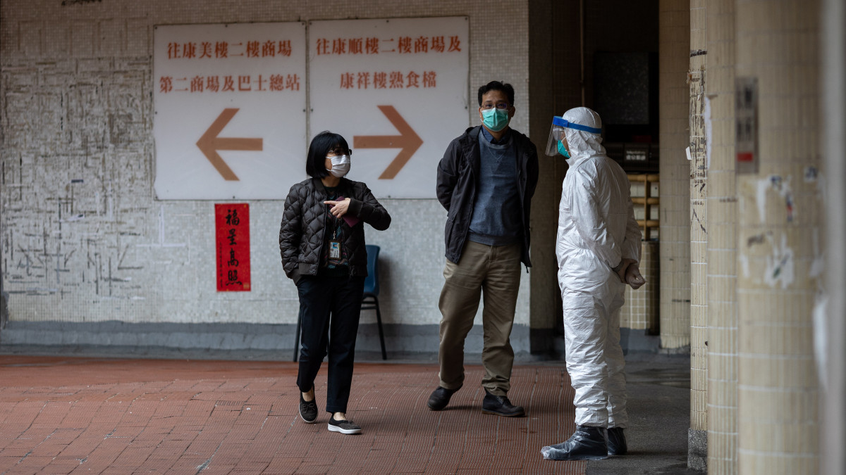 Védőruhás rendőrtől érdeklődnek lakók a hongkongi Hong Mej társasház előtt 2020. február 11-én, miután két lakó szervezetében kimutatták az új koronavírust, emiatt pedig a többi lakót evakuálták és karanténba helyezték. Hongkongban 42-re emelkedett a fertőzöttek száma.