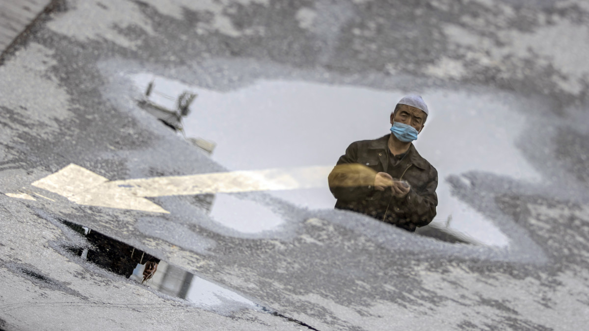 Védőmaszkos férfi képe tükröződik egy pocsolyában, a kuangcsoui központi pályaudvarnál 2020. február 12-én. A koronavírus előidézte tüdőgyulladás halálos áldozatainak száma 1114-re emelkedett Kínában, a legtöbben a járvány gócpontjában, Hupej tartomány székhelyén, Vuhanban hunytak el.