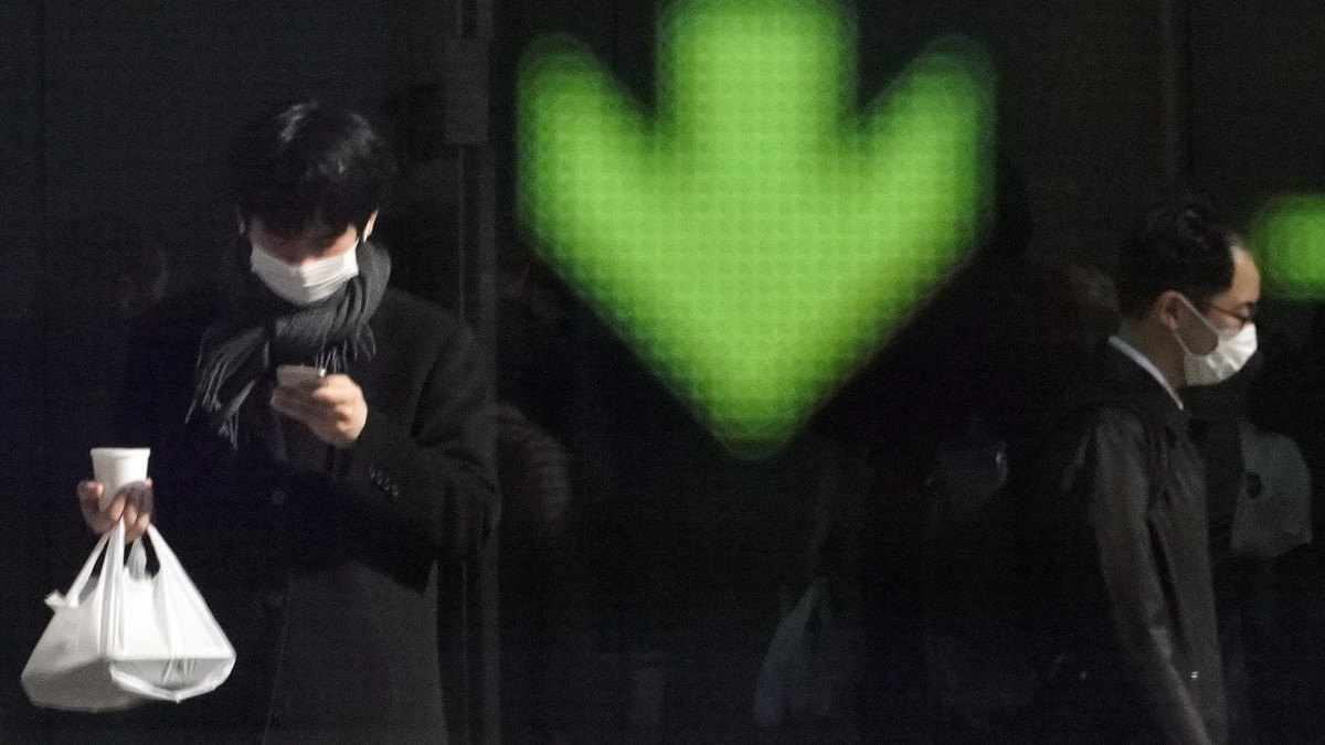 Maszkot viselő járókelők a tokiói tőzsde kijelzője előtt 2020. február 3-án. Tokióban a 225 válogatott részvény Nikkei mutatója 1,09 százalékos veszteségben zárt. Az új koronavírus globális kereskedelemre gyakorolt hatása miatt esnek az ázsiai indexek.