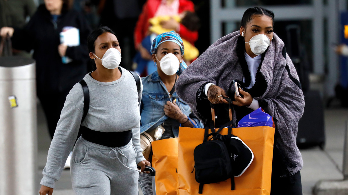 Jamaicából érkező, védőmaszkot viselő nők a New York-i John F. Kennedy nemzetközi repülőtéren 2020. március 12-én. A tüdőgyulladást okozó koronavírus világméretű terjedése miatt Donald Trump amerikai elnök az előző nap bejelentette, hogy az Egyesült Államok harminc napra felfüggeszt minden beutazást Európából, ez azonban nem vonatkozik a Nagy-Britanniából érkezőkre.