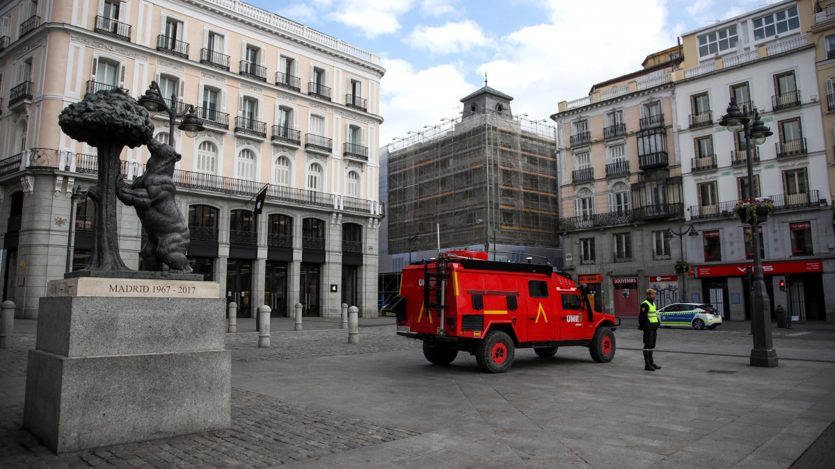 A spanyol hadsereg vészhelyzeti alakulatának tagjai járőröznek a madridi Napkapu téren, a Puerta del Solon 2020. március 17-én, a koronavírus-járvány terjedése miatt bevezetett szükségállapot harmadik napján. A korlátozó intézkedések szerint csak a munkába járás és az alapvető szükségleti cikkek beszerzése miatt lehet utcára lépni, a szabályszegőket  megbírságolják. Balra a Madrid címerállata szobor: az eperfa gyümölcséért kapaszkodó mackó.